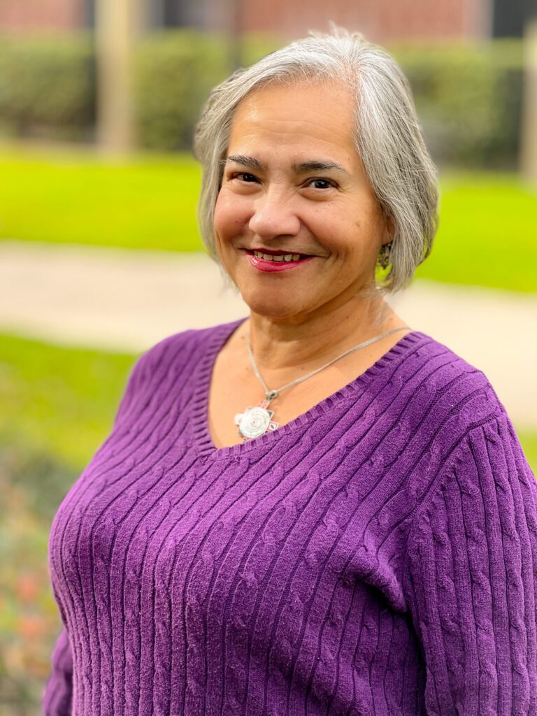 White haired woman in a bright purple sweater smiling at the camera