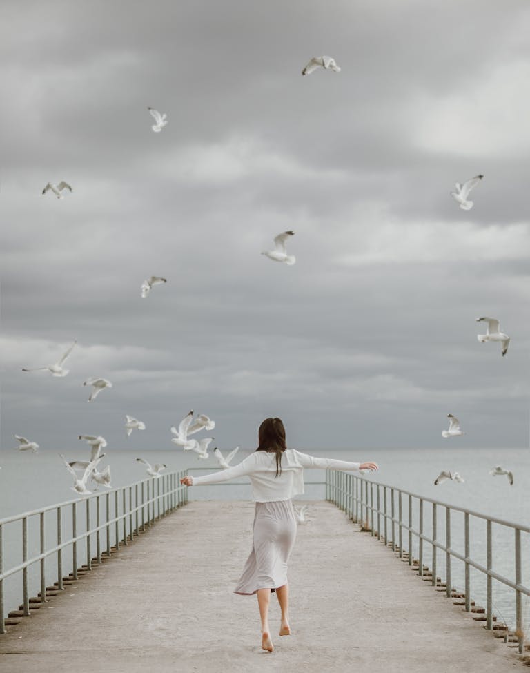 A woman joyfully walking barefoot on a dock surrounded by soaring seagulls, symbolizing freedom.